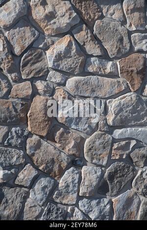 random oddly shaped natural stones or rocks exterior stone wall or rock wall mason built retaining wall of home exterior masonry vertical background Stock Photo