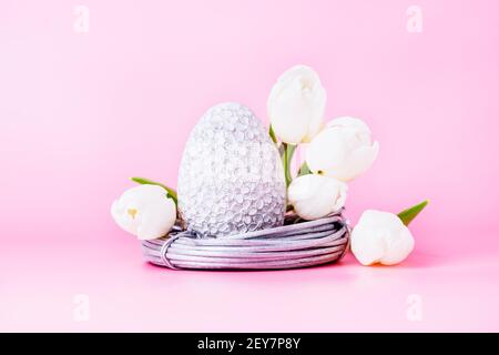 Grey easter egg in the nest and white tulips on a pink background Stock Photo