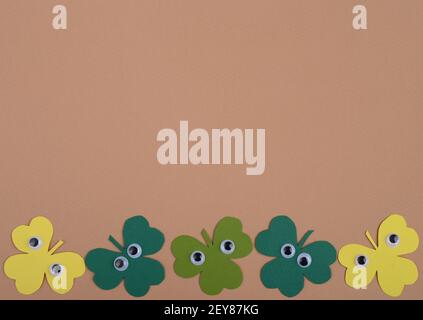 St Patricks Day paper shamrocks with cartoon plastic eyes on beige background.  Flat lay, top view. Stock Photo