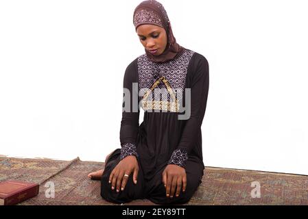 young muslim woman sitting in long dress on mat praying. Stock Photo