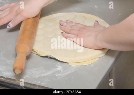 Cook rolls out dough with wooden rolling pin on mold for making dumplings. Cooking homemade ravioli. Stock Photo