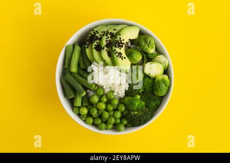 Vegan poke bowl with white rice and green vegetables in the white  bowl in the center of the yellow background.Top view.Closeup. Stock Photo