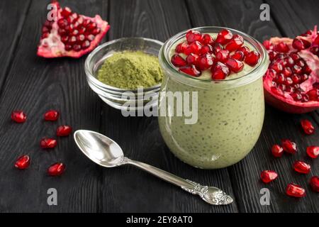 Pudding with chia, matcha tea and pomegranate seeds in the glass jar on the black wooden background. Closeup. Stock Photo