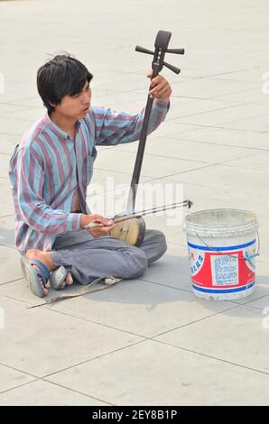 Beijing, China-May 26,2013: A beggar playing the erhu, Chinese traditional instrument, by the street. Selective focus points Stock Photo