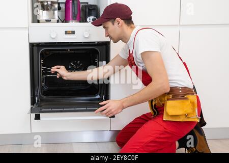 handsome young repairman fixing oven with screwdriver Stock Photo