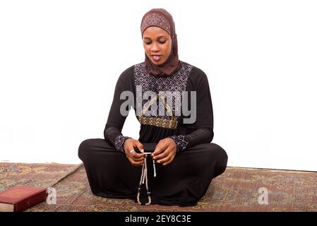 young muslim woman sitting in long dress on mat praying while smiling. Stock Photo