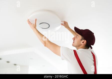 Electrician installs a chandelier on the ceiling. Construction concept Stock Photo