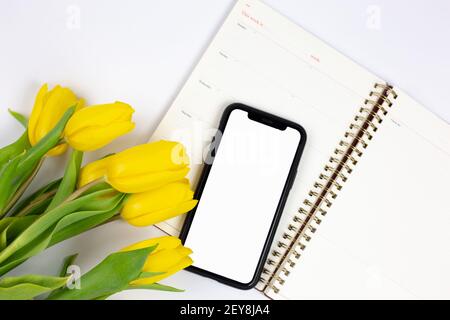 bouquet of yellow tulips and phone lying on a notebook on a white background  Stock Photo