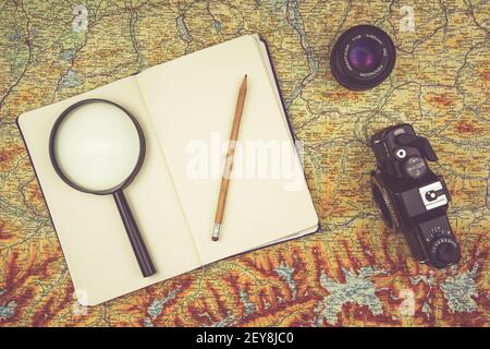 KATOWICE, POLAND - Feb 12, 2021: Notebook with magnifying glass and pencil lying on an old map next to a vintage camera Stock Photo