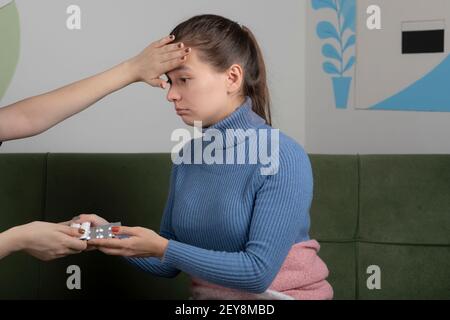Image of sick girl getting check up by her friend while sitting on the sofa Stock Photo
