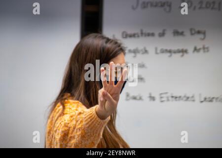 Holding up three fingers, a California elementary school teacher explains three syllable words to her third grade language arts students. Note face mask due to the coronavirus pandemic. Stock Photo