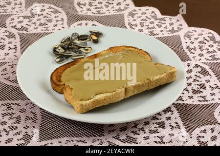Sunflower butter on whole wheat toasted bread with sunflower seeds on white plate withe sunflower seeds on lace table runner Stock Photo