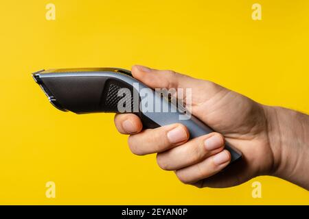 Close up on hand of unknown caucasian man holding electric beard trimmer cordless hair cutter in front of modern yellow background Stock Photo