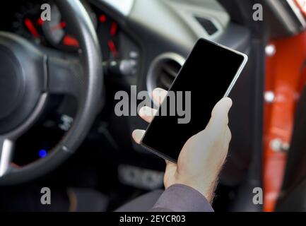 A blank screen mobile phone in the hand of a business man sitting in a sports car. Stock Photo