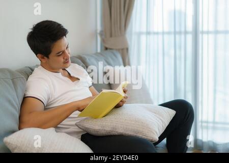 Asian man are sitting reading books, resting on the sofa in the living room in the house. Stock Photo
