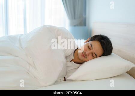 Asian man are sleeping and having good dreams in white blanket in the morning. Rest after work tiring in bedroom at home Stock Photo