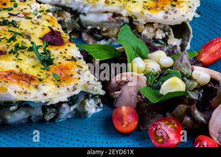 Vegetarian lasagne topped with toasted pine nuts and melting cheeses. With salad and red wine. Stock Photo