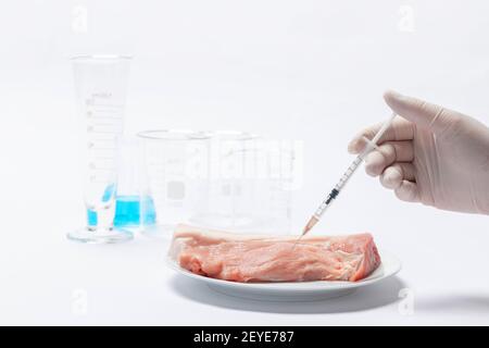 A closeup of a scientist injecting toxic substances to a raw piece of meat on a plate in a laboratory Stock Photo