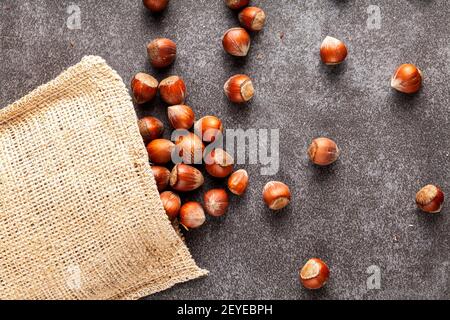 closeup flat lay image of hazelnuts in shells scattered from a vintage burlap sack onto dark background. Some are shelled and some are cracked. A meta Stock Photo