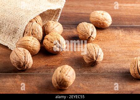 A pile of fresh raw English Walnuts scattered on a wooden table out of burlop vintage  bag. A rustic image  with close up selective focus on walnuts i Stock Photo