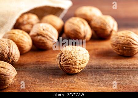 A pile of fresh raw English Walnuts scattered on a wooden table out of burlop vintage  bag. A rustic image  with close up selective focus on walnuts i Stock Photo