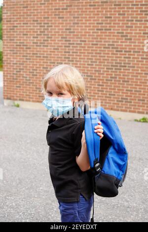 Little child in mask during corona virus outbreak. Little kid wearing mask and carrying backpack, going to school. Back to school concept after reopen Stock Photo