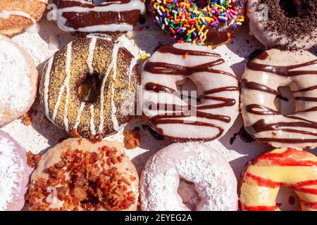Closeup angled image of fresh made store bought donuts in paper box fresh out of the donut shop. An assortment with different flavors and toppings are Stock Photo