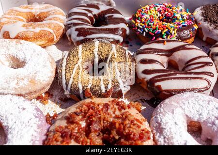 Flat lay image of fresh made store bought donuts in paper box fresh out of the donut shop. An assortment with different flavors and toppings are packe Stock Photo