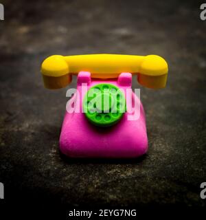 A colorful toy telephone with a green dial and yellow handset placed on a dark surface in a playful setting Stock Photo