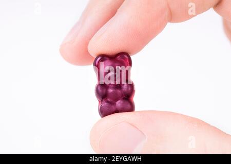 Crop view of male fingers holding a purple gummy bear against white background. Stock Photo