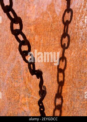 A close-up view of old, rusted chains against a textured orange background highlighting their intricate shapes Stock Photo