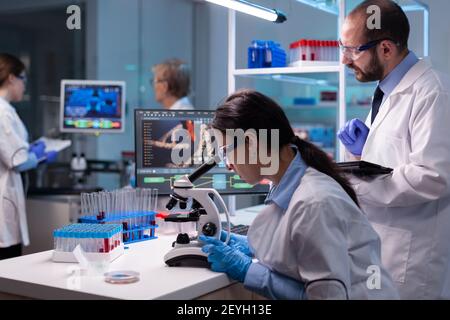 Team of medical research scientists analyzing virus disease using microscope in equipped laboratory. Doctor and chemists examening vaccine evolution, working at diagnosis development. Stock Photo