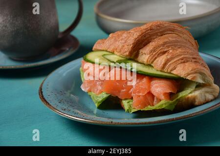 Crispy croissant with salmon and lettuce and cucumbers. Tasty breakfast. Stock Photo