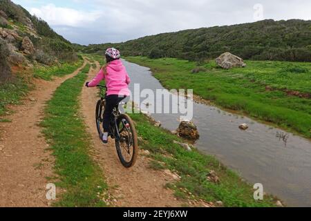 Girl on mountain bike cycling along a dirt track next to a river Stock Photo