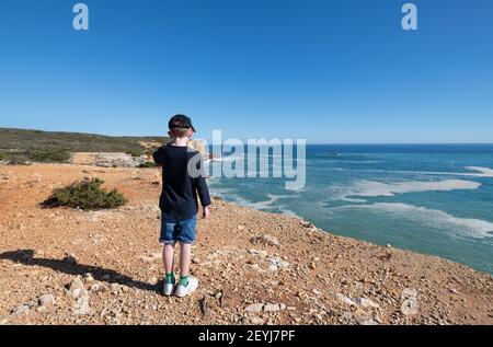 Young boy standing on a coastal footpath looking out to sea Stock Photo