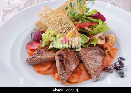 Slices of meat with vegetables and mushrooms, on a white plate Stock Photo