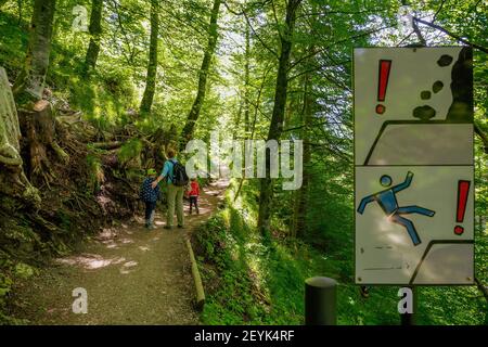 Family passed information sign aside a hiking trail deep in the Bavarian forest warning hikers not to leave the trail and to watch for falling rocks Stock Photo