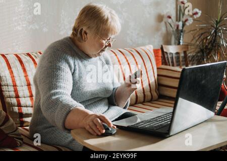Senior woman Holding Credit Card near laptop at home. Mature woman shopping online, using credit card and laptop, make online payment Stock Photo