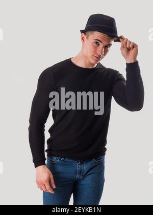 Young man tipping his hat, touching fedora hat on his head, in studio Stock Photo