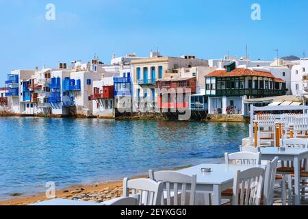 Beautiful Little Venice, Mykonos, Greece. Romantic neighborhood with whitewashed bars, cafes, restaurants. Colorful tables and chairs by shoreline Stock Photo