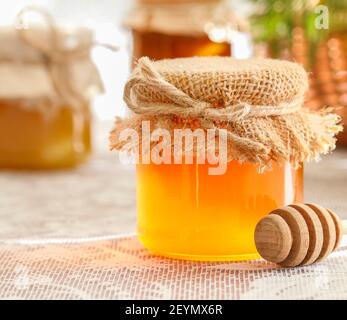 Glass jars with honey on the table and sunflowers in the background. Healthy food Stock Photo