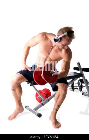 Muscular blond young man lifting weights and listening to music in headphones Stock Photo