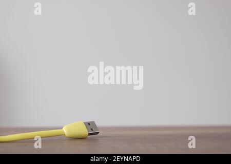 Yellow colored USB type cable staying on dark wooden table with isolated wall background. Stock Photo