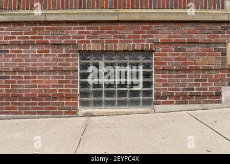 Straight on view of a glass block basement window in an old red brick building, sloping sidewalk foreground, horizontal aspect Stock Photo