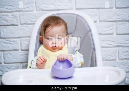 Premium Photo  A small child sits on a highchair and eats food from a  plate with a spoon. baby silicone utensils for feeding babies