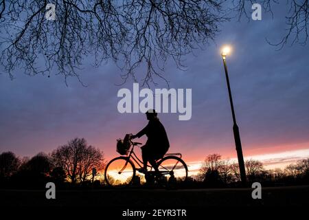 A cyclist rides through a London park at sunset under  street light Stock Photo