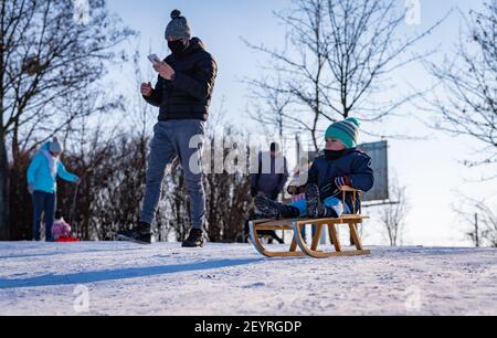 POZNAN, POLAND - Jan 17, 2021: Adults and kids having fun with sleds and snow on a hill at a park on a cold winter day. Stock Photo