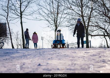 POZNAN, POLAND - Jan 17, 2021: Adults and kids having fun with sleds and snow on a hill at a park on a cold winter day. Stock Photo