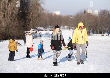 POZNAN, POLAND - Jan 17, 2021: Adults and kids walking with a sled on white snow at a park on a cold winte Stock Photo