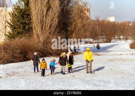 POZNAN, POLAND - Jan 17, 2021: Adults and kids walking with a sled on white snow at a park on a cold winte Stock Photo